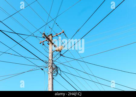 Poteau électrique avec fils désordonnés contre le ciel bleu Banque D'Images