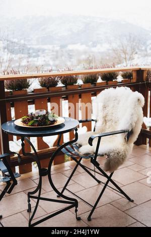 Balcon d'hiver avec table basse, chaise confortable recouverte de fourrure blanche et vue splendide sur les montagnes enneigées.Vacances d'hiver Banque D'Images