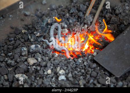 Pièce de forge d'art dans le charbon de bois d'un feu de forge dans une forge au forgeron Banque D'Images