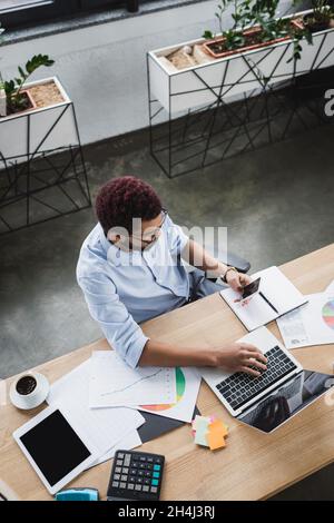 Vue aérienne de l'homme d'affaires afro-américain utilisant des gadgets près des documents dans le bureau Banque D'Images