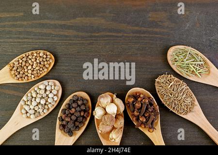 Vue de dessus d'un assortiment d'épices aromatiques et d'herbes dans des cuillères en bois sur fond de bois brun foncé Banque D'Images