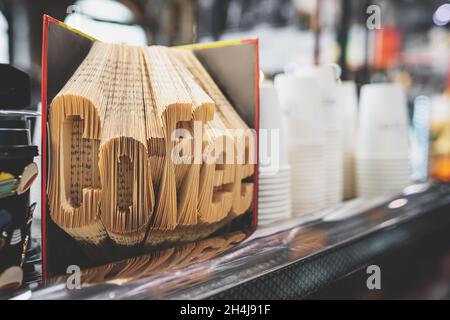 Café Word avec pages de livre pliées.Livre la décoration de sculpture dans un confortable café-restaurant intérieur.Gobelets en papier blanc sur l'arrière-plan.Image teintée avec mise au point sélective.Concept commercial de café à emporter Banque D'Images