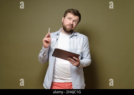 Un homme beau avec une tablette et un stylet est en réflexion sur une idée, il est réfléchi et incertain.fond vert. Banque D'Images