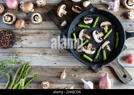 Asperges et champignons fraîchement coupés dans une poêle en fonte. Banque D'Images