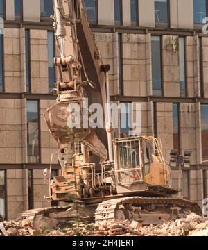 digger travaille à la démolition de vieux bâtiments avec de nouveaux bâtiments en arrière-plan. Banque D'Images