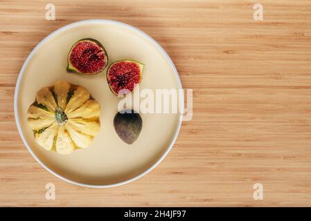 Figues mûres fraîches et petite citrouille sur plaque jaune sur table en bois.Concept de Thanksgiving.Vue de dessus, plat, espace de copie. Banque D'Images