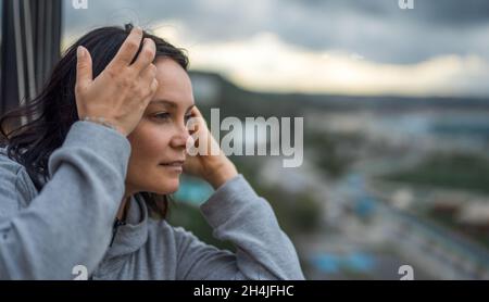 une femme heureuse d'âge moyen regarde joyeusement et avec assurance dans la distance d'une hauteur de fenêtre. copier l'espace Banque D'Images