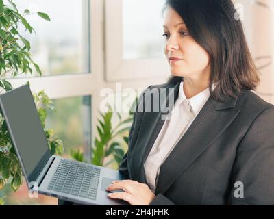 femme d'affaires tenant un ordinateur portable.Femme mature tenant les mains d'un ordinateur portable travaillant en ligne sur un ordinateur portable sur fond de fenêtre Banque D'Images