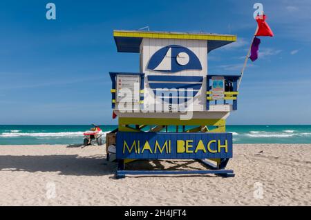 Un gros plan d'une station de garde de plage en bois avec des drapeaux et le texte 'Miami Beach'; en arrière-plan l'océan Atlantique et une moto à quatre roues Banque D'Images