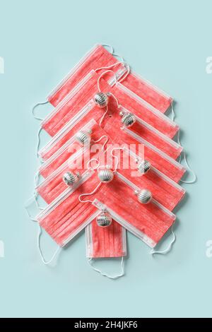 Arbre de Noël alternatif fait de masques médicaux de visage et de boules de vacances d'argent sur fond bleu.Protection contre les virus.Vue de dessus.Mi créatif Banque D'Images