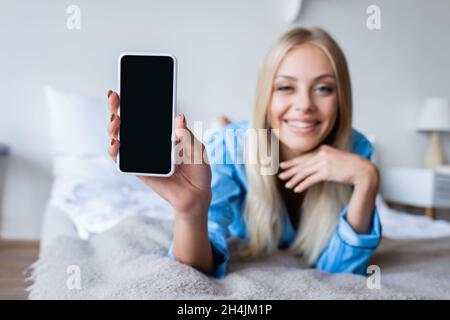 femme floue et heureuse en pyjama tenant un smartphone avec écran vide dans la chambre Banque D'Images