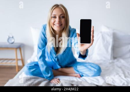 femme ravie floue en pyjama tenant un smartphone avec écran vide dans la chambre Banque D'Images