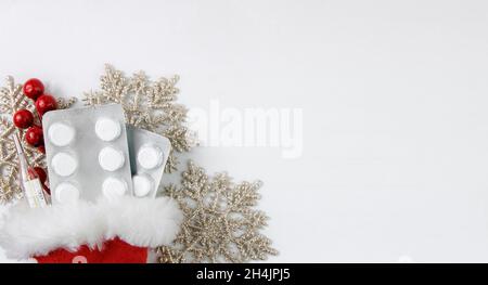 Contexte médical de Noël.Pilules, blister, thermomètre, dans chapeau de père noël, sur fond blanc avec flocons de neige.Bannière.Plat.Copier l'espace Banque D'Images