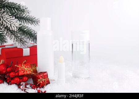 Bouteilles de cosmétiques pour le soin de la peau sur une surface enneigée.Cosmétiques d'hiver.Contenants vierges avec cadeaux et brindilles en toile de fond.Cadeau de Noël pour Banque D'Images