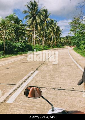 Réflexion dans un miroir d'aile de deux femmes sur un scooter roulant le long de la route, Philippines Banque D'Images