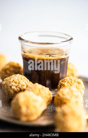 Boules de bonbons maison enrobées de noix hachées avec une tasse de café noir Banque D'Images