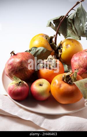 Pésimmon et autres fruits dans une plaque isolée sur fond blanc.Directement au-dessus. Banque D'Images