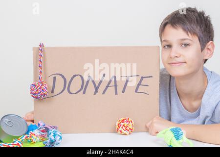 Enfant souriant tenant un morceau de carton brun avec inscription Don et dessins de chats et d'un chien.Bénévoles collectant un don pour un animal Banque D'Images