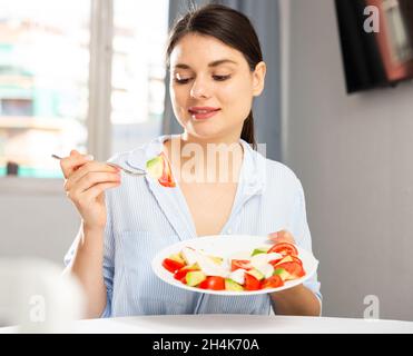 Portrait d'une jeune femme souriante mangeant de la salade et prenant le déjeuner à la maison Banque D'Images