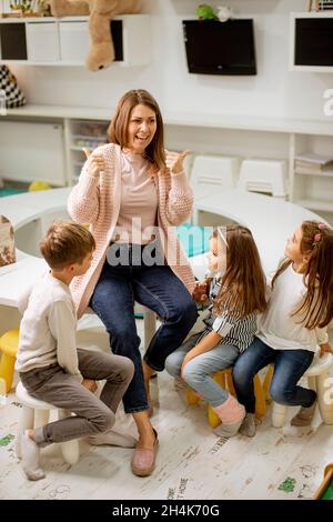 Un professeur de maternelle parle de l'histoire à un groupe d'enfants assis sur une petite chaise à la maternelle Banque D'Images