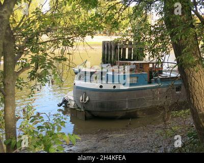 London alternative style de vie: Une ancienne péniche, ombragée par des arbres, amarrée sur le côté sud de la Tamise juste à l'ouest de Kew Bridge. Banque D'Images