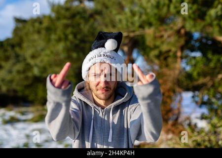 Un jeune homme grincheux portant un chapeau de père noël noir avec les mots Bah Humbug écrits dessus Banque D'Images