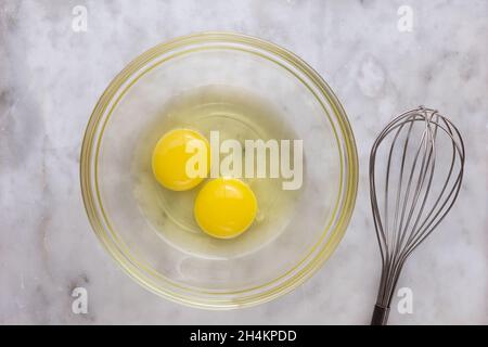 Vue de dessus de deux jaunes et blancs crus dans un bol en verre et fouetter sur la surface en marbre Banque D'Images