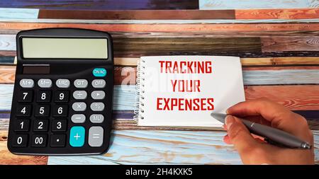 Texte suivi de vos dépenses, écrit dans un bloc-notes avec un stylo main femelle, à côté d'une calculatrice Banque D'Images