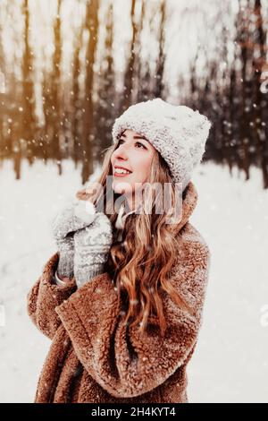 Belle jeune femme dans une forêt enneigée d'hiver.Fille portant des gants, une casquette et un manteau molletonnés.Forêt de Noël, arbres sur fond flou.Croisé Banque D'Images