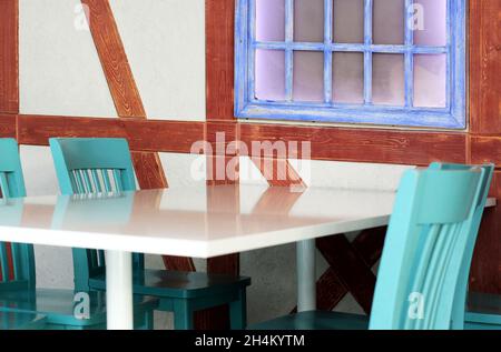 Café avec chaises en bois vert, table blanche et fenêtres brunes. Banque D'Images