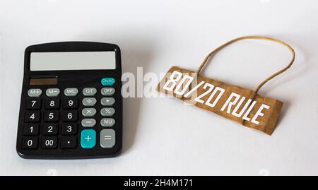 Sur fond blanc, une étiquette de prix sur papier avec le texte règle 80 20, à côté de celle-ci, est une calculatrice Banque D'Images