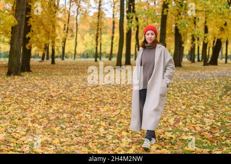 Portrait d'une femme marchant dans un manteau de laine et un chapeau rouge au parc d'automne Banque D'Images