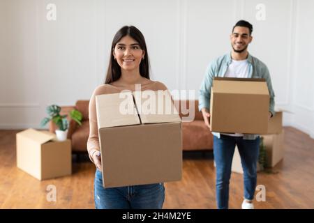 Concept de relocalisation.Bonne dame millénaire tenant une boîte en carton marchant dans une nouvelle maison, jeune famille de deux personnes se déplaçant dans l'appartement acheté, excitée Banque D'Images