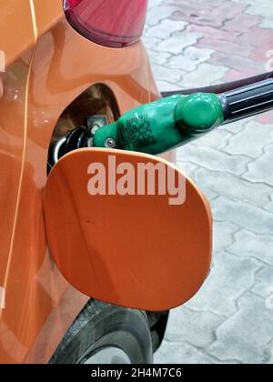 photo verticale montrant un injecteur d'essence sans plomb vert qui remplit de carburant diesel dans une voiture orange montrant cette source d'énergie qui disparaît rapidement Banque D'Images