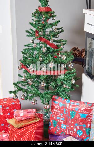 Cadeaux de Noël enveloppés de papier coloré sous l'arbre de Noël décoré de balles et de ruban rouge Banque D'Images