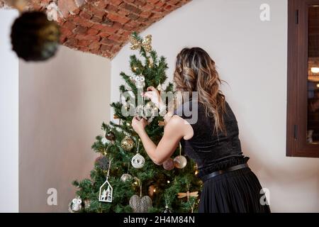 Belle jeune femme blonde du dos décorant l'arbre de Noël avec des ornements dorés faits à la main Banque D'Images