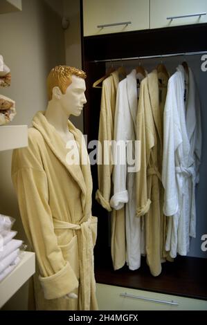 Une photo de beaucoup de robes de chambre sur des cintres en bois dans un magasin et un mannequin mâle dans une robe de chambre à côté. Banque D'Images