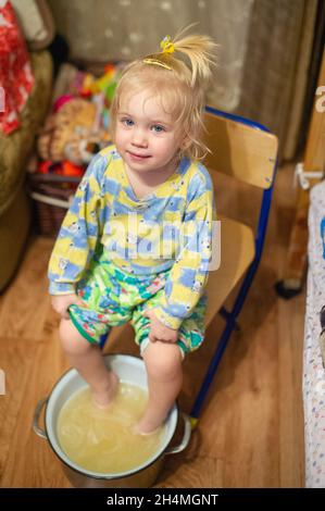 La fille attrapé un froid s'assoit à la maison et est traitée en utilisant l'eau chaude dans un bassin. Banque D'Images