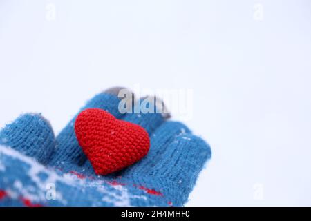 Coeur rouge sur la paume de la main dans un gant tricoté chaud contre la neige.Concept d'amour romantique, Saint-Valentin ou charité Banque D'Images