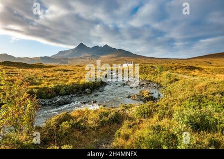 Chalet blanc isolé (Allt Dearg House) à Glen Sligachan avec les montagnes Black Cuillin au-delà et la banque de nuages sombres au-dessus, île de Skye, Écosse. Banque D'Images