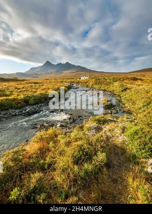 Chalet blanc isolé (Allt Dearg House) à Glen Sligachan avec les montagnes Black Cuillin au-delà et la banque de nuages sombres au-dessus, île de Skye, Écosse. Banque D'Images