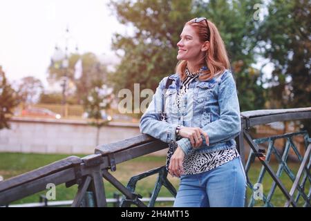 Jeune femme caucasienne positive à tête rouge regardant le pont dans le parc Banque D'Images