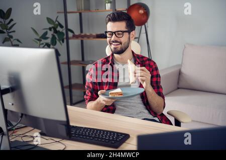 Portrait d'un sympathique gars tendance et gai mangeant des en-cas frais faits maison regardant la télévision sur Internet au bureau poste de travail intérieur Banque D'Images