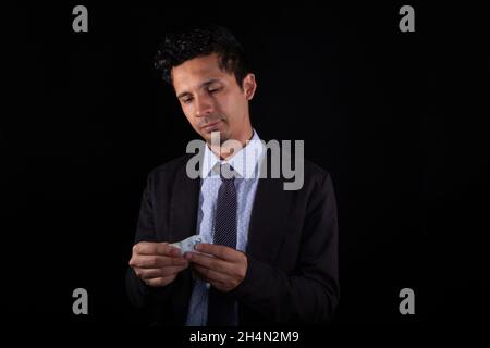 Homme d'affaires comptant de l'argent, isolé sur fond noir.Jeune latin homme portant des vêtements élégants comptant des factures d'argent.Jeune adulte latin jeune homme. Banque D'Images