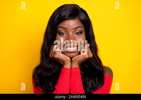 Photo de la peau sombre douce rêveuse fille vêtue rouge haut bras joues isolé couleur jaune arrière-plan Banque D'Images