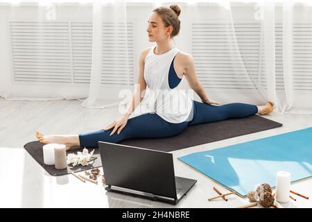 Gros plan jeune fille sportive de forme ne pratique la vidéo en ligne de formation hatha yoga sur un ordinateur portable moderne.Elle est assise en position et médite.Studio de yoga.En bonne santé Banque D'Images