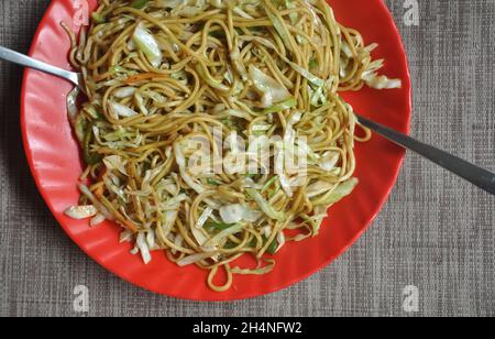 Vue panoramique sur le chow mein (cuisine chinoise) servi dans une assiette de couleur rouge dans le café Banque D'Images