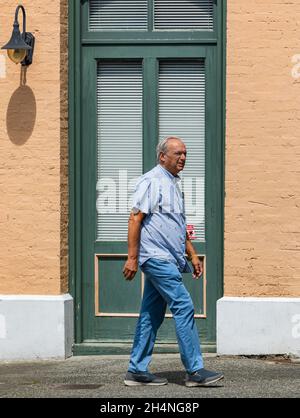 Un homme de haut niveau qui marche le long du trottoir le long de la rue.Un homme marche sur le trottoir à l'arrière-plan de l'ancien bâtiment.Photo de rue Banque D'Images