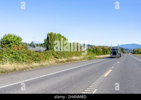 Puissant tracteur semi-remorque industriel noir classique transportant une semi-remorque à plateau vide, sur la route de l'autoroute jusqu'à l'entrepôt Banque D'Images