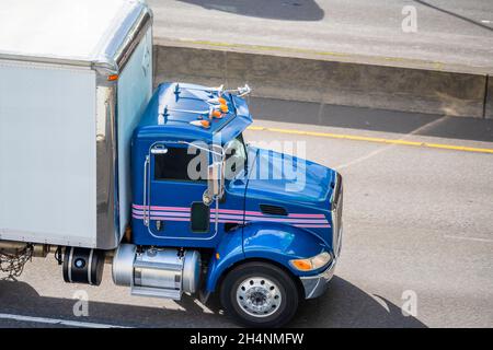 Utilisation professionnelle de qualité industrielle, bleu vif, puissant tracteur semi-remorque à cabine de jour de classe moyenne avec remorque à plateau sur la voie publique Banque D'Images